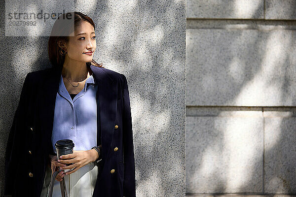 Eine Frau in blauem Hemd und Jacke lehnt an einer Wand