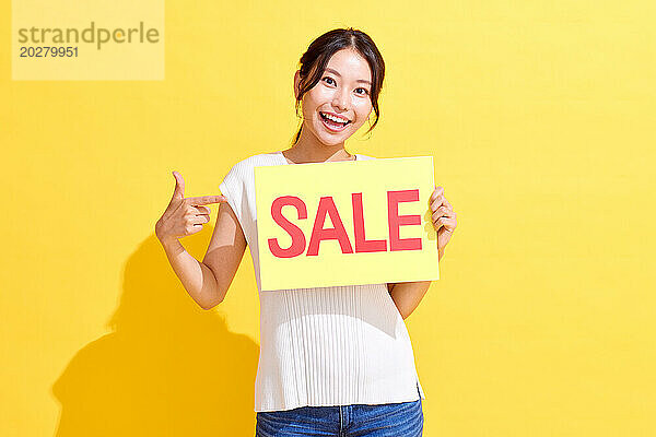 Glückliche asiatische Frau hält ein Verkaufsschild auf gelbem Hintergrund