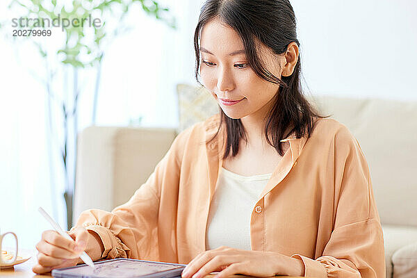 Asiatische Frau schreibt auf Tablet  während sie am Tisch sitzt