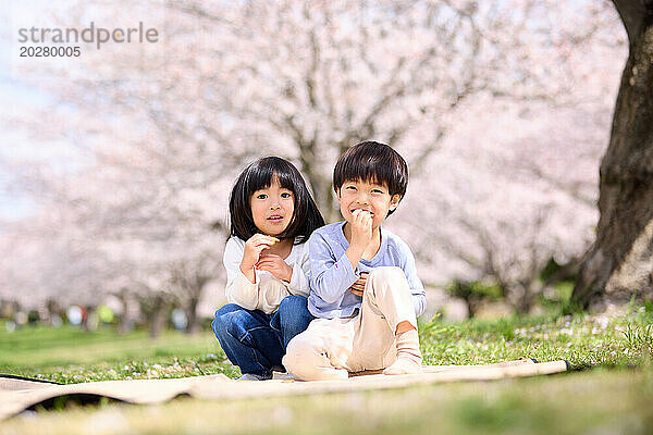 Zwei Kinder sitzen im Gras und essen einen Apfel