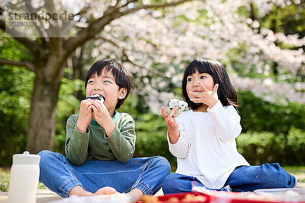 Zwei Kinder sitzen auf einer Decke und essen Reisbällchen