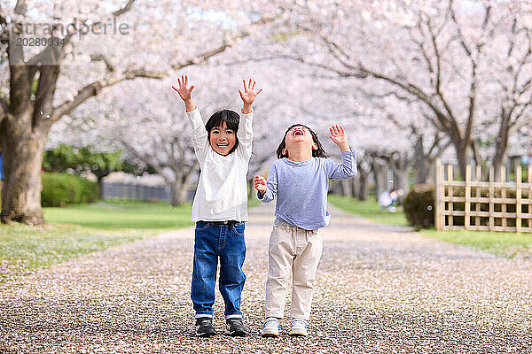Zwei Kinder stehen mit erhobenen Händen vor einem Baum