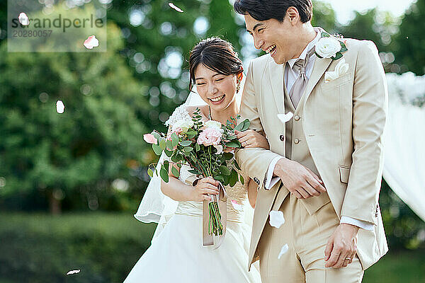 Ein frisch verheiratetes Paar geht mit fallenden Blütenblättern durch ein Feld