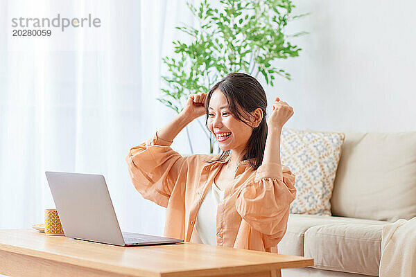 Asiatische Frau sitzt mit Laptop auf der Couch und lächelt