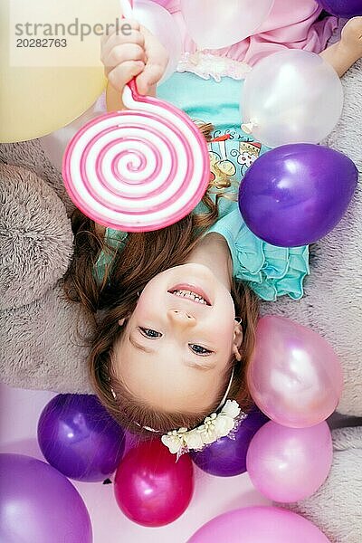 Draufsicht auf ein fröhliches kleines Mädchen  das mit Luftballons posiert