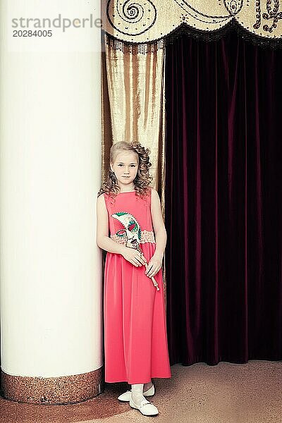 Hübsches blondes Mädchen posiert im langen roten Kleid am Eingang zu Szenen