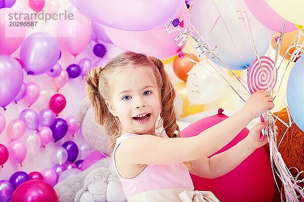 Fröhliches kleines Mädchen posiert mit einem Bündel von bunten Luftballons