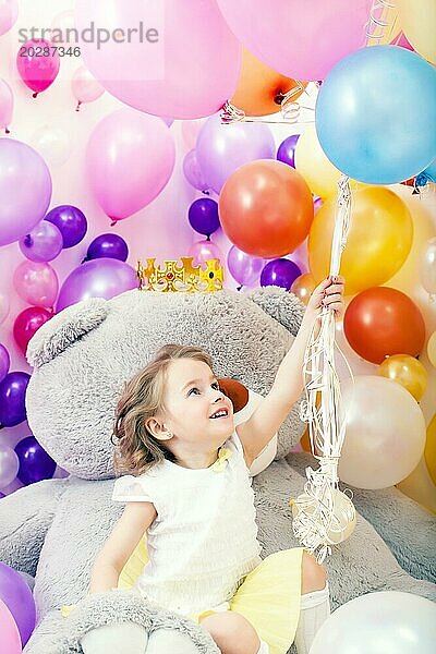 Fröhliches kleines Mädchen packt ein Bündel bunter Luftballons