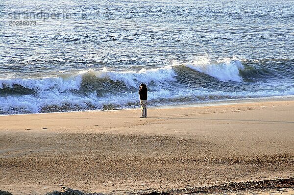 Eine Person steht allein am Strand und blickt auf das Meer  umgeben von Wellen und Sand im Dämmerlicht  bei Mindelo  Porto  Nordportugal  Portugal  Europa