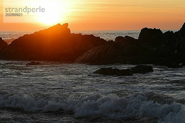 Die Silhouetten von Felsen stehen im Kontrast zu den Wellen des Meeres unter einem orange gefärbten Himmel bei Sonnenaufgang  bei Mindelo  Porto  Nordportugal  Portugal  Europa