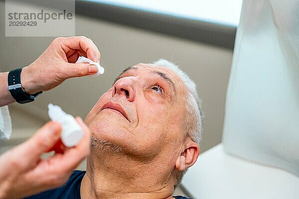 Ein Augenarzt gibt einem Mann vor einem Glaukomtest mit einem Lasergerät Tropfen zur Erweiterung der Pupille ins Auge