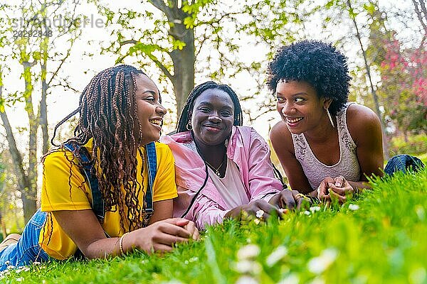 Drei junge afrikanische Freundinnen  die in einem Park liegen und sich entspannt unterhalten und den Frühlingstag genießen