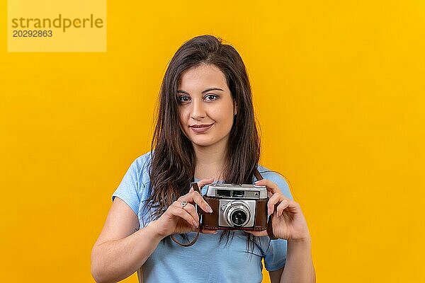 Studio Porträt mit gelbem Hintergrund einer Frau  die eine Retro Fotokamera in den Händen hält