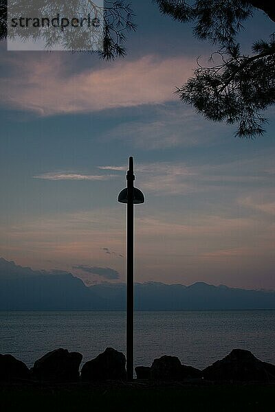 Silhouetten voneiner Straßenlaterne und Zweigen vor Dämmerungshimmel  Berge und Gardasee im Hintergrund  Sirmione  Gardasee  Italien  Europa