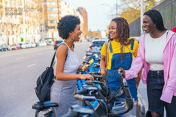 Drei afrikanische junge glückliche Freunde mieten ein öffentliches Fahrrad und benutzen ein Telefon in der Stadt
