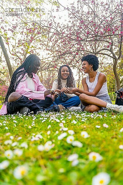 Vertikale Bodenperspektive von drei jungen afrikanischen Freundinnen  die einen schönen Frühlingstag im Park genießen und mit Blumen spielen