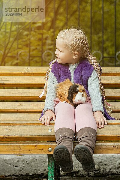 Bild der reizenden kleinen Mädchen sitzen auf der Bank mit ihrem Meerschweinchen