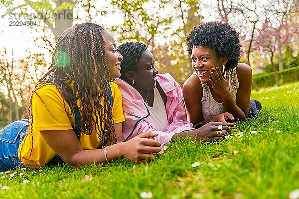 Glückliche drei junge afroamerikanische Frauen liegen in einem Park und genießen den Frühling