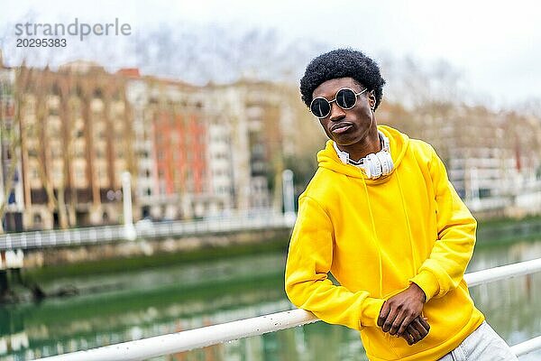 Porträt mit Kopiervorlage eines selbstbewussten  coolen afrikanischen jungen Mannes mit Sonnenbrille an einem Fluss in der Stadt