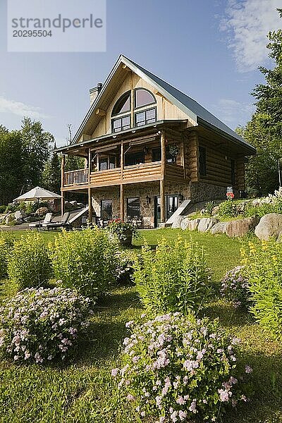 Handgefertigtes zweistöckiges Blockhaus aus Fichtenholz mit Feldsteinschornstein und grünem Blechdach in Sommer  Quebec  Kanada  Nordamerika