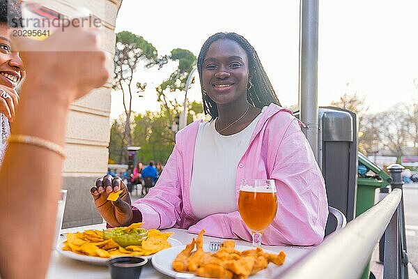 Lächelnde afrikanische junge Frau isst Nachos mit Freunden in einem Restaurant im Freien