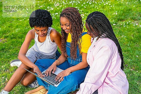 Draufsicht auf drei junge afrikanische Studentinnen  die gemeinsam einen Laptop benutzen und in einem Park sitzen