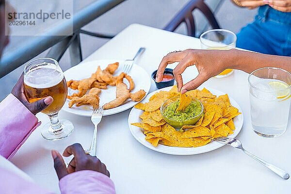 Hände einer Frau  die einen Nacho in Guacamole Soße taucht und eine Mahlzeit mit Freunden in einem Restaurant genießt