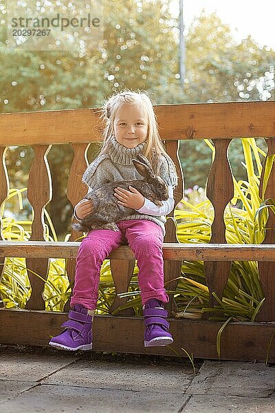 Lächelndes kleines Mädchen posiert in einer Gartenlaube mit Kaninchen  Nahaufnahme