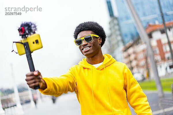 Ein junger afrikanischer Influencer  der mit einem auf einem Stativ befestigten Handy und einem Mikrofon live in der Stadt sendet