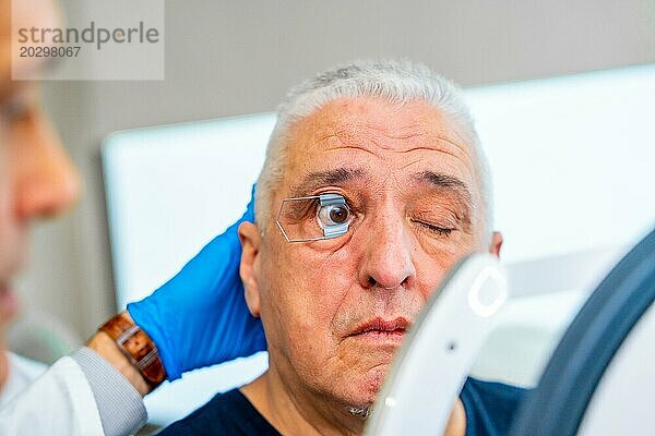 Augenarzt  der ein Werkzeug anwendet  um das Auge eines Mannes für die Untersuchung geöffnet zu halten