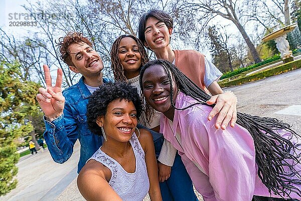 Frontales Dreiviertelporträt von fünf niedlichen jungen gemischtrassigen Freunden  die ein Selfie in einem Park machen