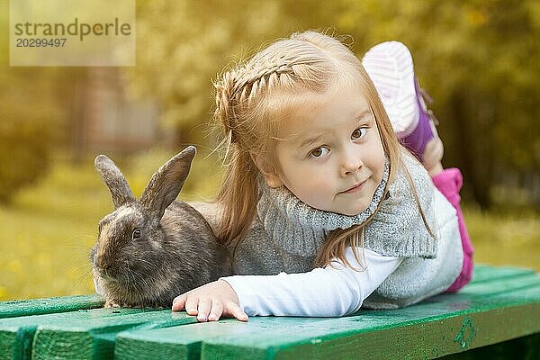 Niedliches braunäugiges Mädchen auf Bank liegend mit Kaninchen  Nahaufnahme