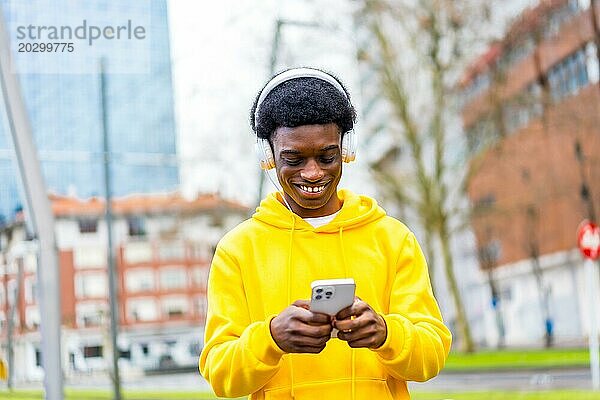 Cooler und fröhlicher afrikanischer junger Mann  der mit seinem Handy in der Stadt Musik hört