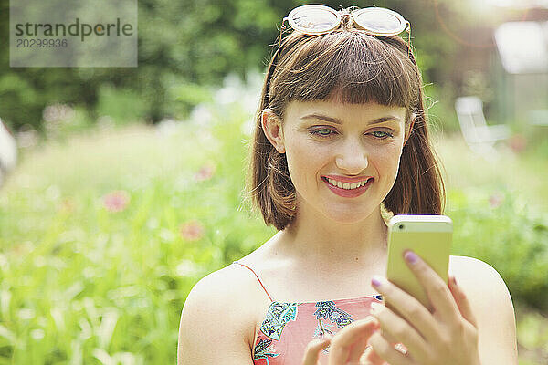 Nahaufnahme eines lächelnden Teenager-Mädchens  das im Freien sein Smartphone benutzt