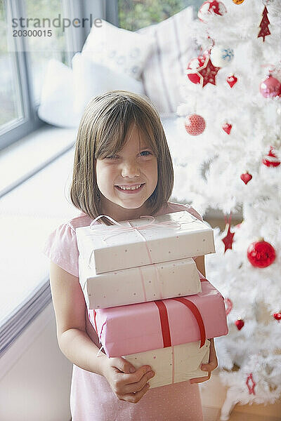 Lächelndes junges Mädchen  das einen Stapel Weihnachtsgeschenke hält