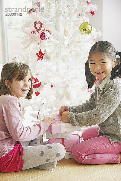 Zwei junge Mädchen öffnen Geschenke unter dem Weihnachtsbaum und lächeln