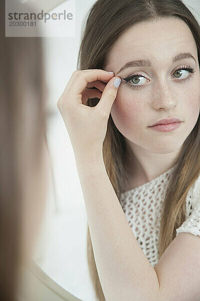 Teenager-Mädchen schaut in den Spiegel und überprüft das Augen-Make-up