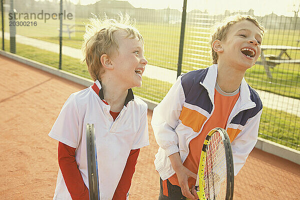 Zwei Jungen halten lächelnd Tennisschläger in der Hand