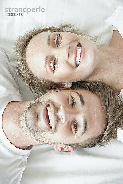 Lächelndes Paar liegt auf dem Bett und blickt in entgegengesetzte Richtungen