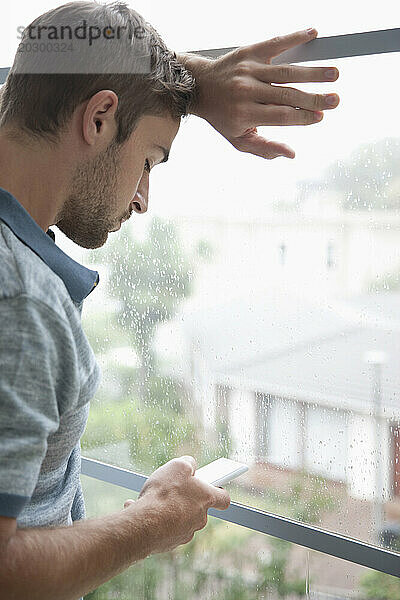 Mann lehnt mit Smartphone am Fenster