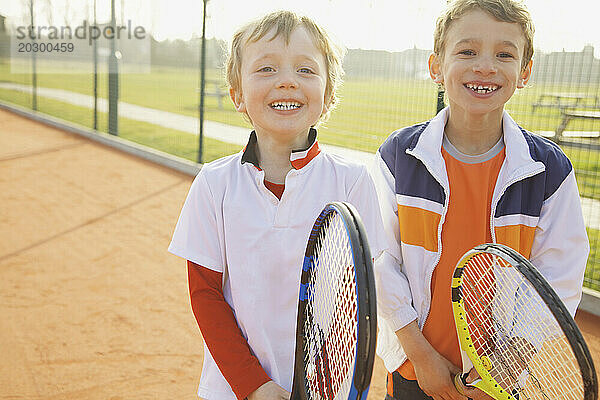 Zwei Jungen halten lächelnd Tennisschläger in der Hand