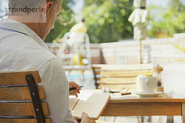Rückansicht eines Mannes  der im Café im Freien auf einem Notizblock schreibt