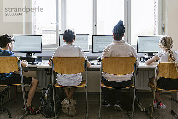 Rückansicht männlicher und weiblicher Schüler  die Computer benutzen  während sie im Klassenzimmer der Schule sitzen