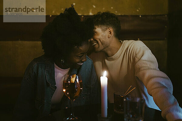 Fröhliches gemischtrassiges Paar  das sich beim Candlelight-Date an der Bar amüsiert