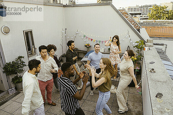 Eine Gruppe unbeschwerter männlicher und weiblicher Freunde tanzt beim Feiern während der Dinnerparty auf dem Balkon