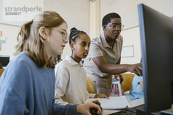 Lehrerin erklärt Schülern am Computer im Klassenzimmer der Schule