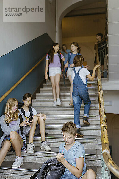 Gemischtrassige männliche und weibliche Schüler auf der Treppe während der Pause in der Schule