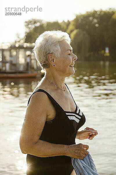 Lächelnde ältere Frau im Badeanzug  während sie im Urlaub am See steht
