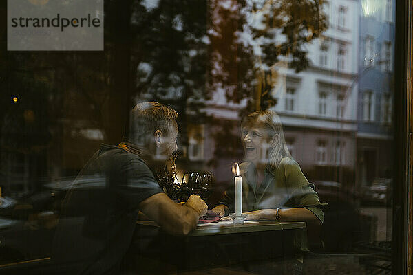 Glückliches älteres Paar  das Spaß beim Date im Restaurant hat und durch Glas gesehen wird