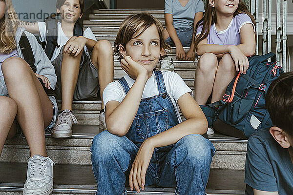 Nachdenkliches Mädchen stützt sich auf den Ellbogen  während es mit Freunden in der Schule auf der Treppe sitzt